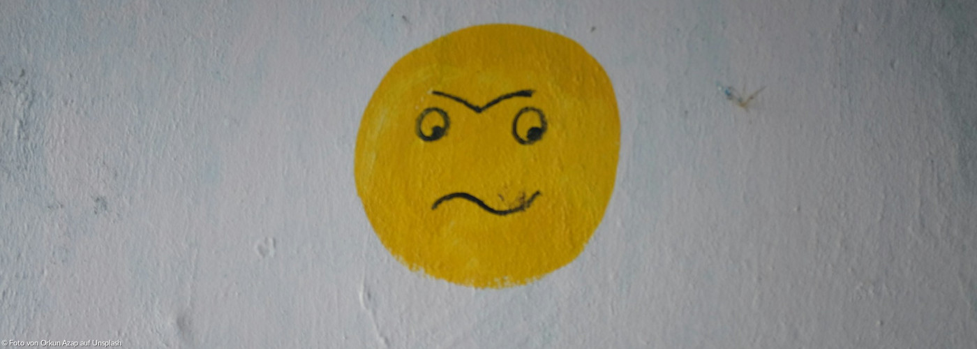 Ein gelbes schlecht-gelauntes Smiley-Gesicht, auf einer weißen Wand