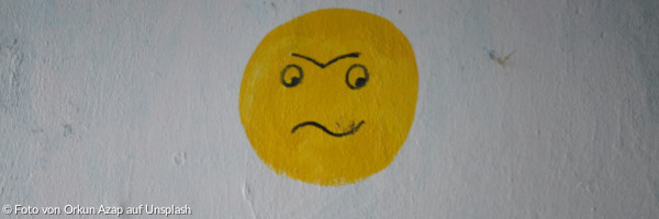 Ein gelbes schlecht-gelauntes Smiley-Gesicht, auf einer weißen Wand